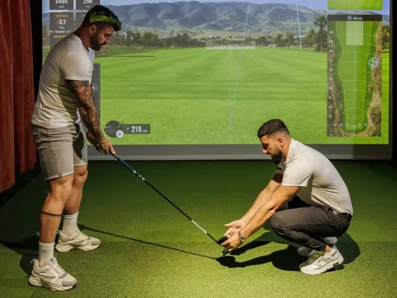 Adultos jugando al golf indoor en un simulador TrackMan en The Clubhouse Marbella, un espacio de deporte y entretenimiento cerca de Puerto Banús.