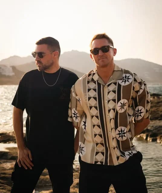 CamelPhat posando junto al mar con gafas de sol, retrato del dúo británico de DJs y productores de house y tech house.