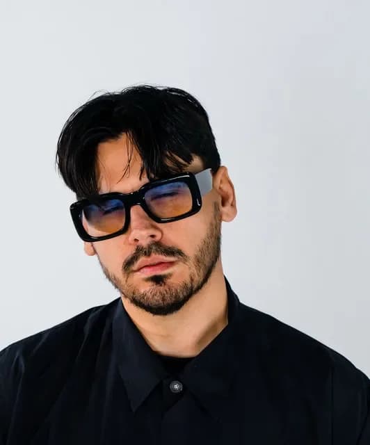 Retrato frontal de KIDDO con gafas oscuras y camisa negra, imagen del productor y artista vinculado a la nueva música urbana española.