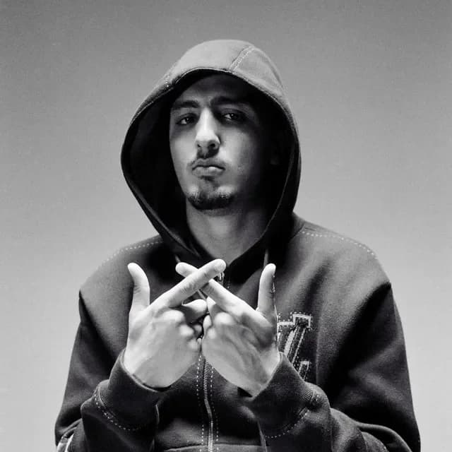 Retrato promocional en blanco y negro de un artista de rap urbano con sudadera y capucha, mirando a cámara y haciendo un gesto con las manos.