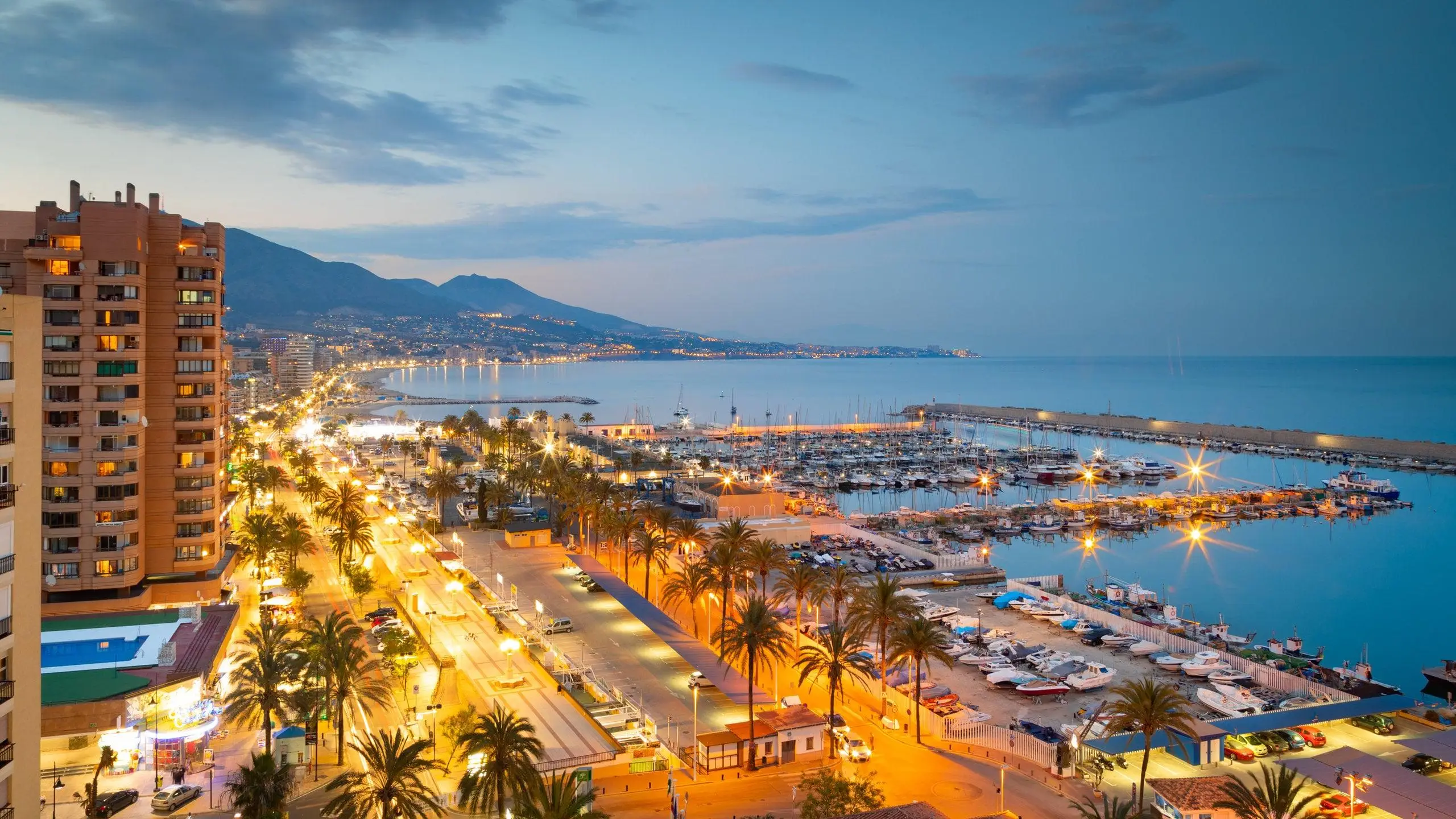 Puerto deportivo y costa de Fuengirola al atardecer con paseo bordeado de palmeras y montañas