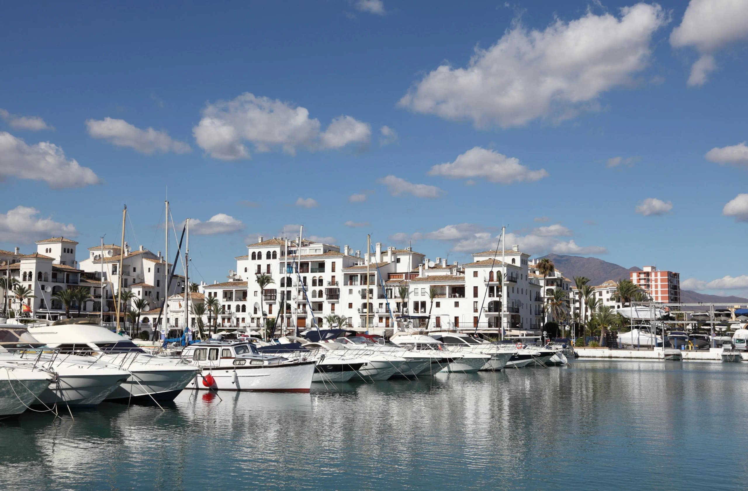 Marina Puerto de la Duquesa en Manilva con yates de lujo, edificios blancos y montañas de fondo