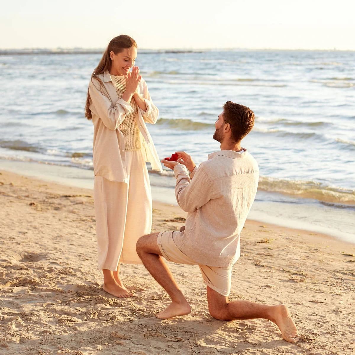 Couple on a beach by the sea, with a man kneeling and presenting a ring to his partner, representing the ¿Y mi anillo pa’ cuándo? experience.