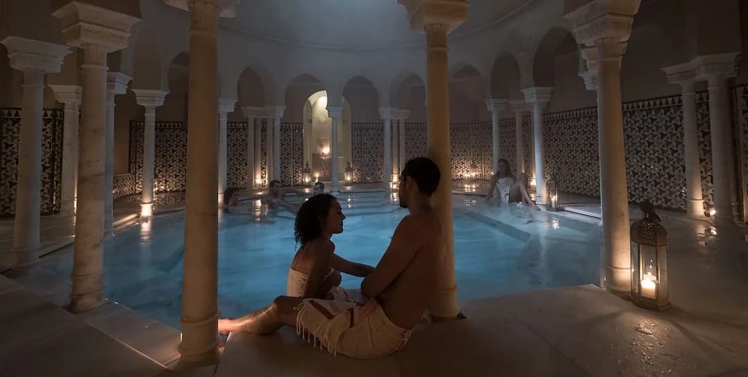 Pareja disfrutando de una experiencia romántica en los baños árabes de Hammam Al Ándalus Málaga, con piscina interior iluminada y ambiente relajante para San Valentín.