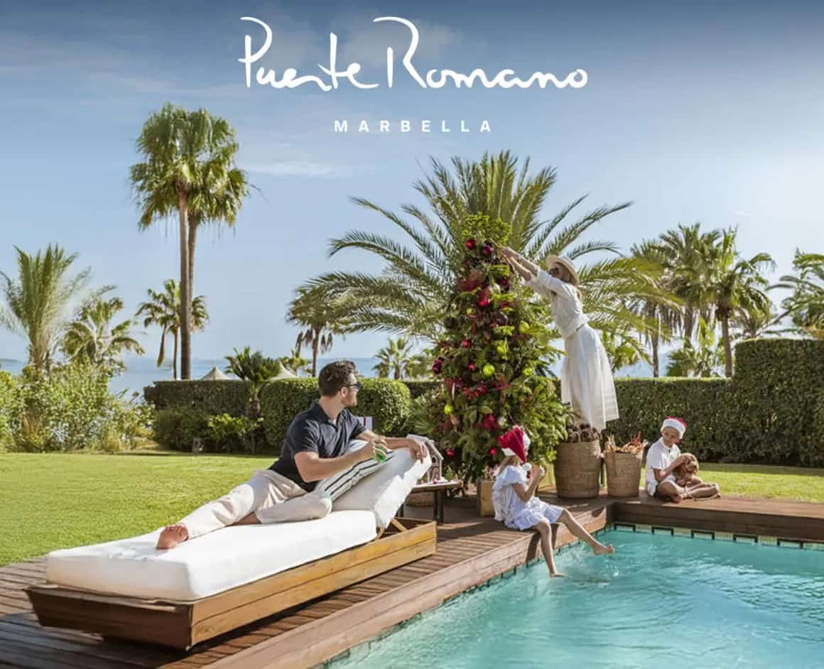 Christmas at Puente Romano Marbella: family by the pool—mother decorating an outdoor tree, children in Santa hats, and father relaxing among palm trees with sea views.
