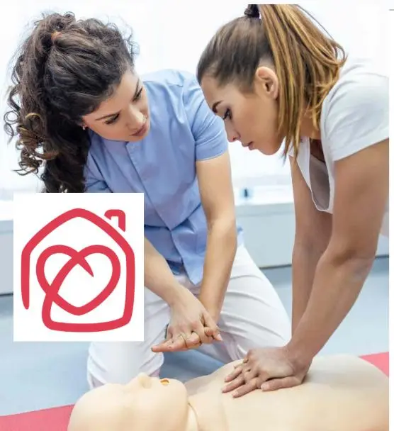 Curso de primeros auxilios en Casa Ángeles, dos mujeres practicando RCP sobre un maniquí con el logo de la asociación en primer plano.