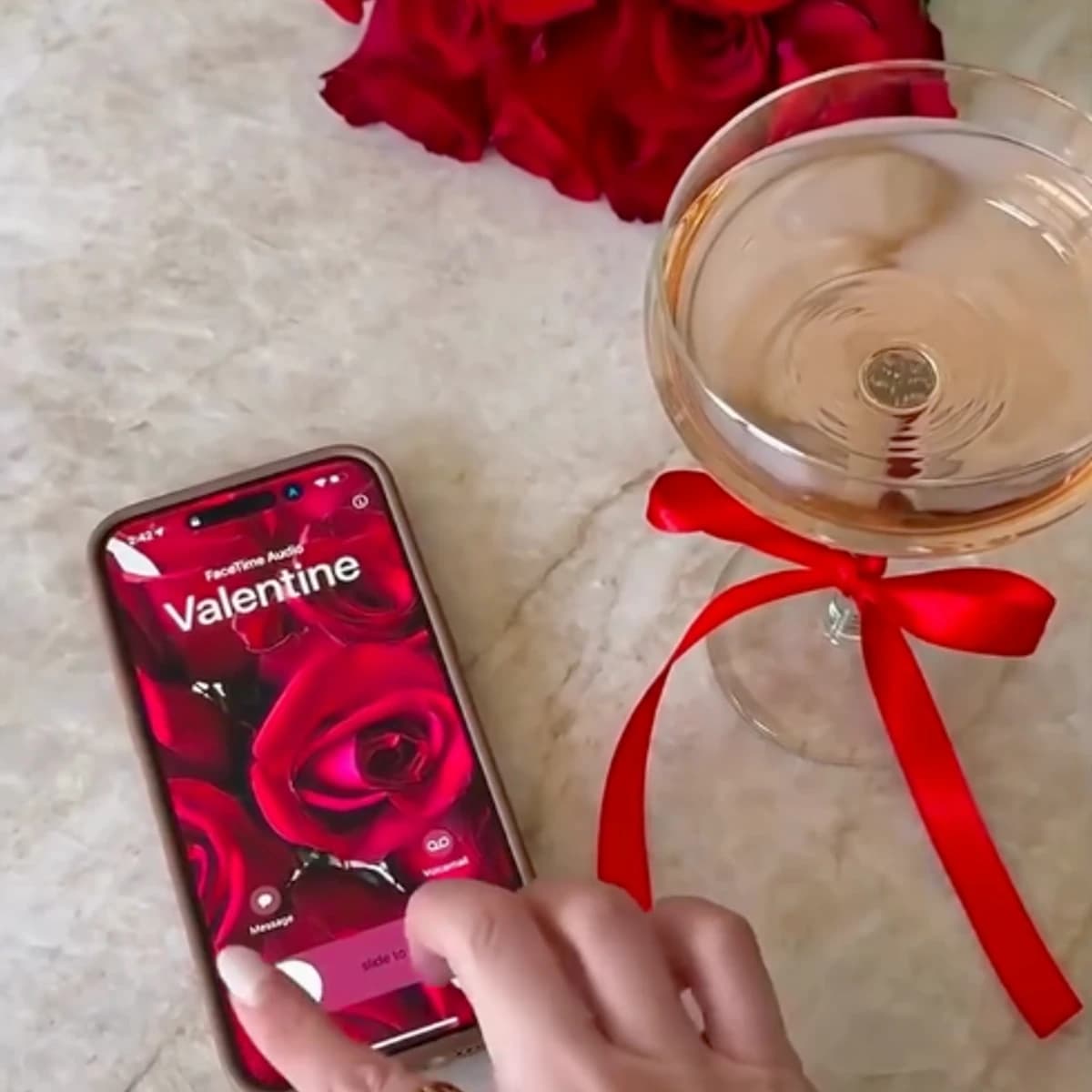 Copa con lazo rojo y móvil con temática romántica junto a rosas rojas, representando una cena especial de San Valentín en Boulebar Café, San Pedro de Alcántara, plan romántico con menú especial.