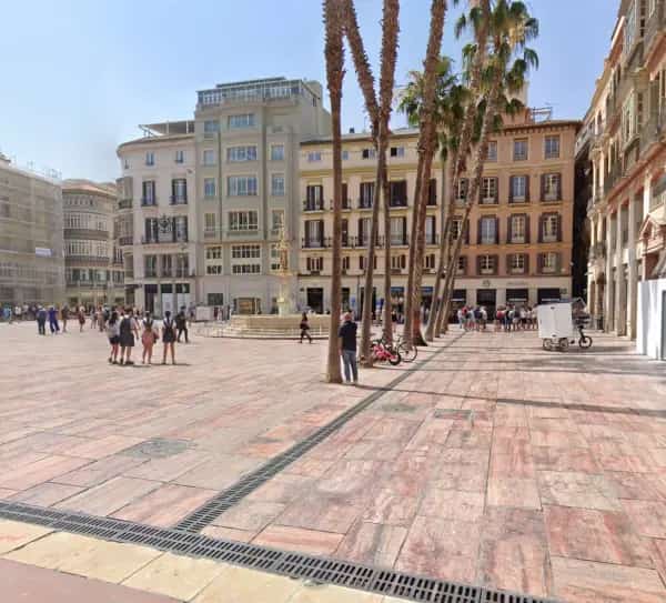 Vista amplia de la Plaza de la Constitución en Málaga con edificios históricos, peatones y cielo despejado en el centro de la ciudad.