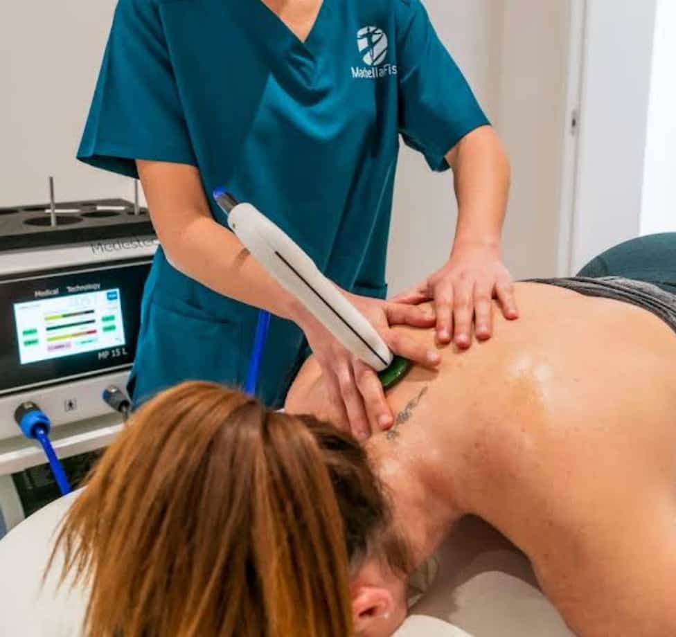 Physiotherapist applying diathermy/wave treatment to a patient’s back using a professional device in the clinic.