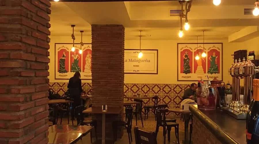 Interior cálido de Taberna La Malagueña con columnas de ladrillo visto y carteles de flamenco vintage en las paredes.