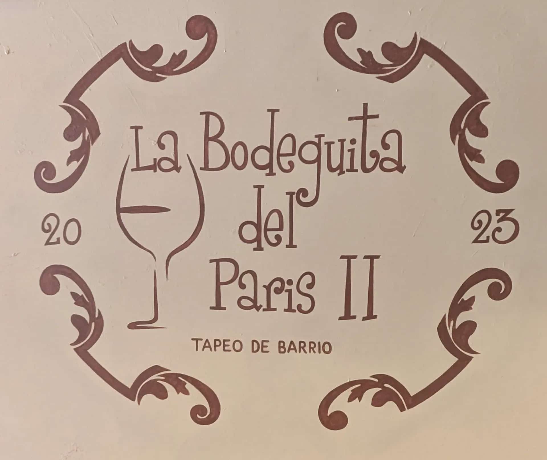 Logo pintado en pared de La Bodeguita del París II con copa de vino y el texto “Tapeo de barrio”, en San Pedro Alcántara (Marbella).