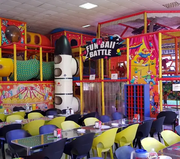 Zona de juegos interior de Kidz Kingdom con estructura multijuego, toboganes, túneles y cartel de “Fun Ball Battle” junto a las mesas de cumpleaños.