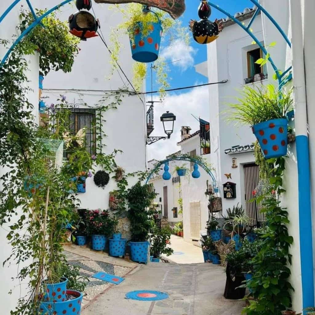 Old town street with blue flowerpots, arches and whitewashed façades in Jubrique.