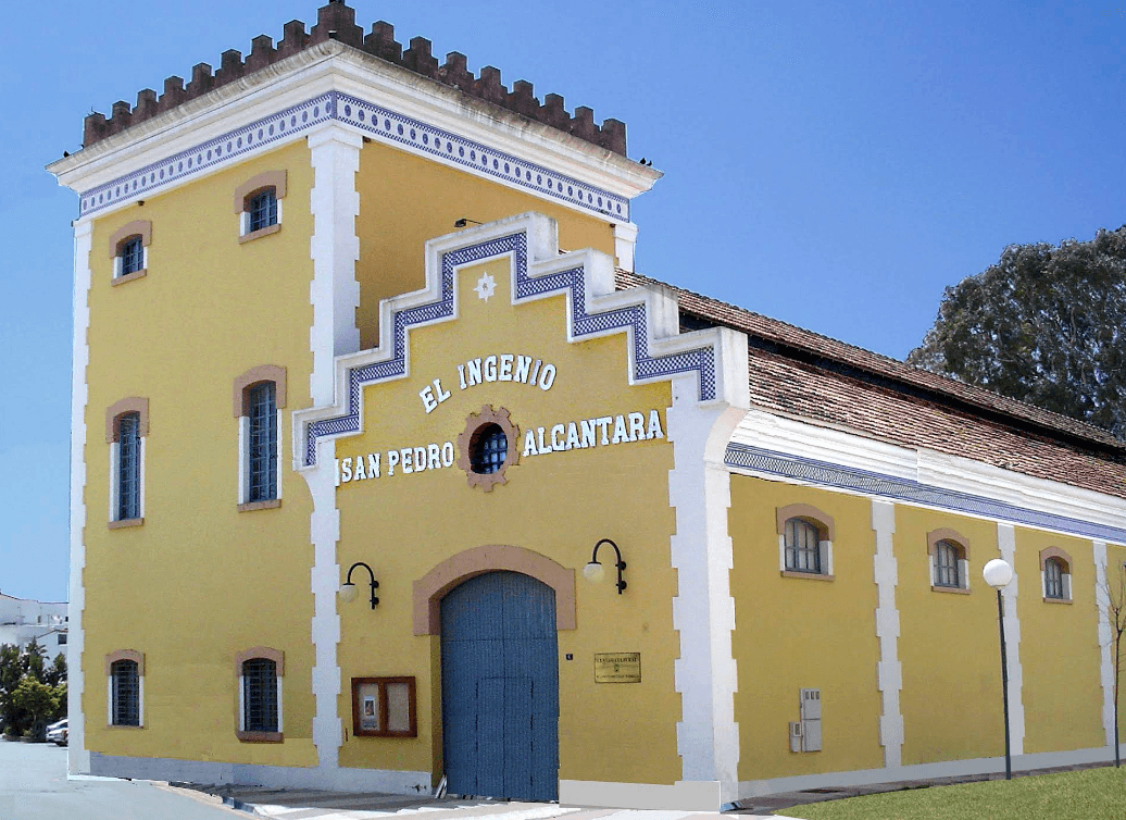 Front yellow façade of the historic El Ingenio building in San Pedro Alcántara, a former sugar mill with a stepped, tiled gable and the sign “El Ingenio San Pedro Alcántara” above a large arched doorway.