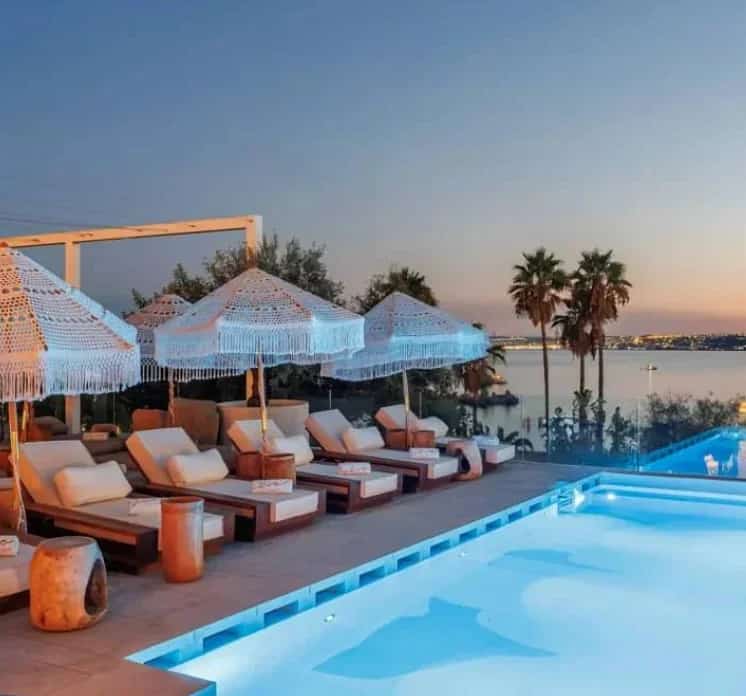 Boho-style sunbeds and parasols by the infinity pool at EVA Estepona Greek Restaurant & Beach Club at dusk, overlooking the sea on Playa del Cristo in Estepona.